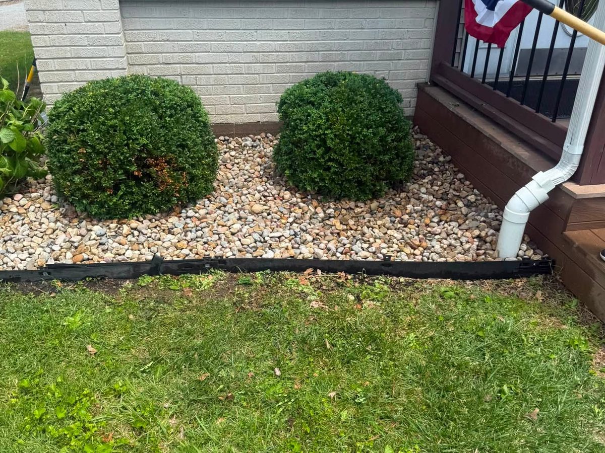 River rock bed with steel edging and trimmed shrubs against a home